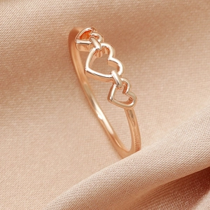 Macro shot of rose gold heart ring with triple hollow heart design on champagne silk
