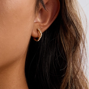Gros plan d'une boucle d'oreille créole dorée avec zircons portée par un modèle