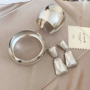 Detailed view of silver textured bangle, smooth bracelet, and geometric earrings set