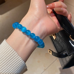 Close-up of blue cat eye stone beaded bracelet worn on wrist with a black handbag