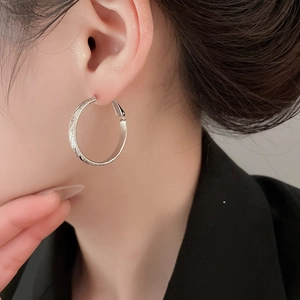 Close-up of silver textured hoop earrings on model highlighting metallic luster