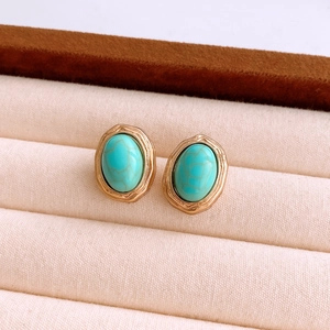 Vue macro de boucles d'oreilles dorées avec pierres turquoise sur tissu beige