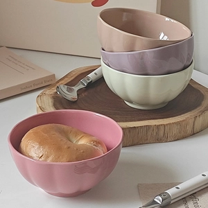 Close-up of pastel ceramic bowls with petal texture and a bagel inside on a desk