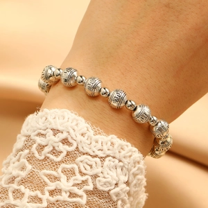 Macro view of silver beaded bracelet featuring Greek key patterns on a satin background