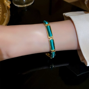 Macro view of gold-plated geometric bracelet featuring rectangular green cat-eye stones
