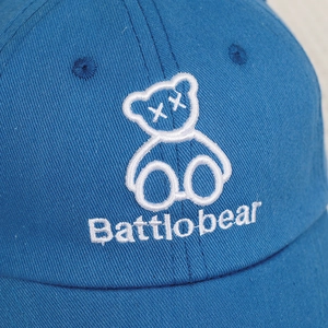 Detail of bright blue cotton baseball cap featuring white embroidered cartoon bear logo