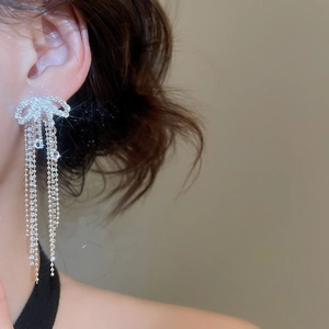 Close-up of sparkling bow knot earrings with long tassels on model's ear
