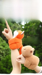 Detail of plush capybara and fox slap bracelets worn on a wrist in an outdoor setting
