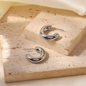 Close-up of silver C-shaped hollow earrings placed on natural beige stone and silk