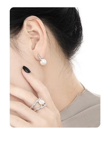 Detailed view of silver twisted ring and pearl earring on a model in soft light