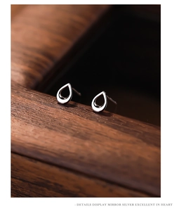 Macro shot of polished silver hollow teardrop earrings on a dark wooden surface