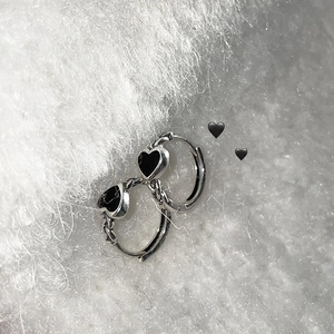 Close-up of silver hoop earrings featuring black heart charms on soft white plush background
