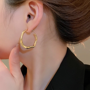 Detailed close-up of a model wearing gold irregular wave hoop earrings with polished finish