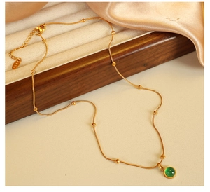 Detail of 18k gold plated beaded chain with vintage green stone pendant on satin fabric