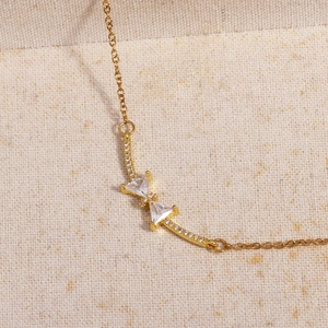 Detailed close-up of golden bow-shaped necklace with sparkling zircons on textured fabric
