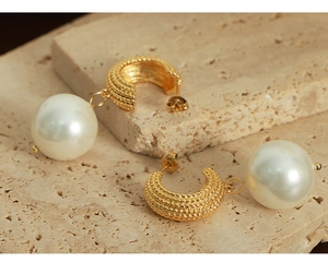 Detail of gold-plated braided metal hoop earrings with elegant white pearl pendant on stone