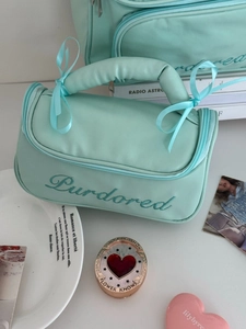 Macro view of mint green leather makeup bag with ribbon bow and embroidered handle