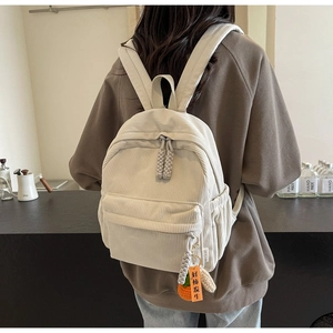 Detailed close-up of cream corduroy backpack texture with a cute persimmon knitted charm