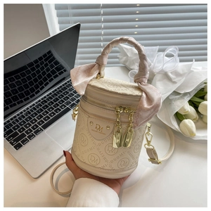 Detail view of cream cylinder bucket bag with embossed logo and silk scarf handle detail
