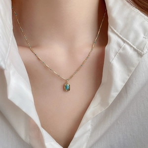 Close-up of bohemian gold chain necklace with square turquoise stone pendant on a model