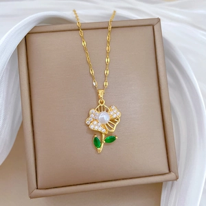 Detail of gold flower necklace with white pearl and green leaf gemstone in a jewelry box