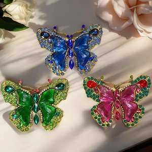 Three vintage crystal butterfly brooches in blue, green, and pink on white silk