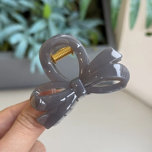 Detail of gray resin bow hair claw clip showing shiny finish and golden metal spring