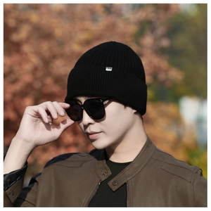 Close-up of black ribbed knit beanie with a silver rectangular metal logo on the cuff
