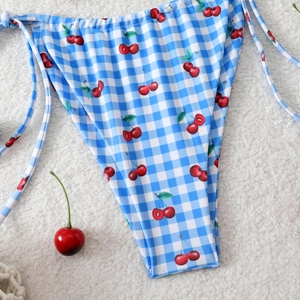 Detail of blue gingham bikini bottom with cherry print and side-tie strings on white rug