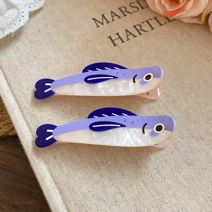 Detail view of purple and white acetate fish hair clips on textured fabric with roses