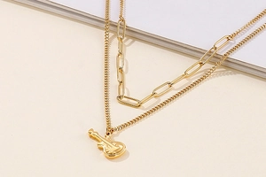 Detailed view of golden double-layer necklace with paperclip chain and guitar pendant