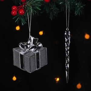 Close-up of clear plastic gift box and icicle ornaments hanging on a pine branch