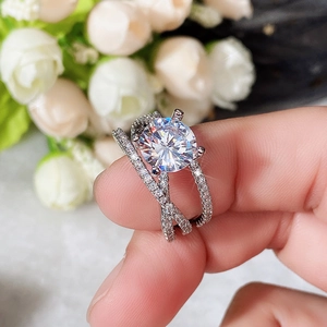 Close-up of a silver four-prong round solitaire ring with a criss-cross diamond-set band