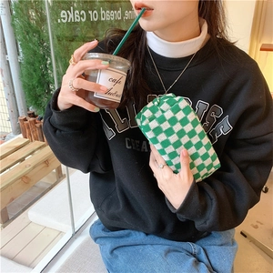 Knitted green checkerboard cosmetic bag held by hand in a cozy cafe setting