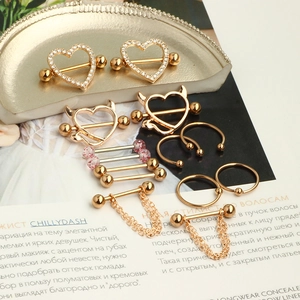 Golden stainless steel nipple rings set with heart and chain designs on a tray