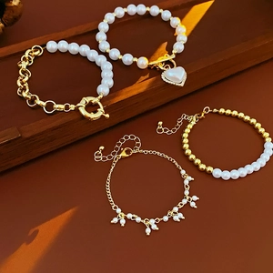 Dettaglio di quattro bracciali di perle e oro con ciondolo a cuore su vassoio di legno