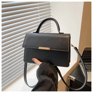 Detail of elegant black leather handbag with premium gold buckle and handle on table
