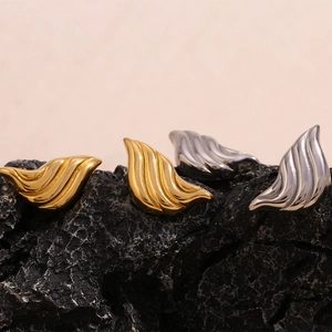 Macro shot of wing-shaped earrings in gold and silver finish on black rock surface