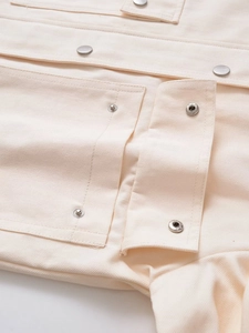 Détail d'une veste utilitaire blanc cassé avec poche à rabat et bouton métallique