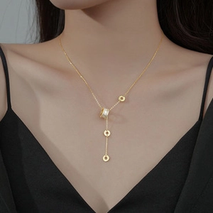 Detailed view of the gold tassel Y-necklace with sparkling cylinder and round metal charms