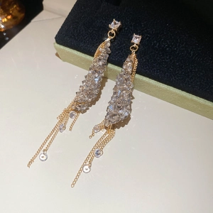 Detail of elegant gold tassel earrings with square crystal studs on green velvet box