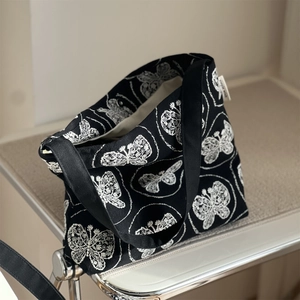 Detail der 3D-Schmetterlingsstickerei und Magnetschnalle an schwarzer Canvas-Tasche