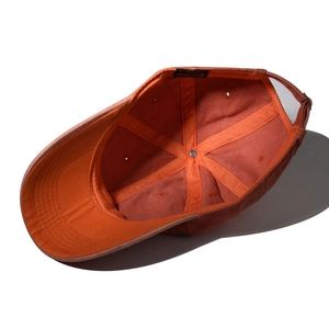 Detailed interior of orange cotton baseball cap showing stitching, sweatband, and eyelets