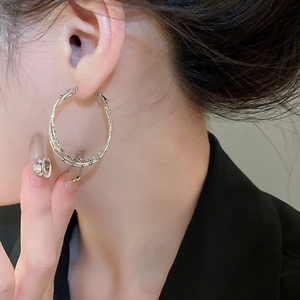 Close-up of a silver twisted geometric hoop earring worn by a model in a professional shot