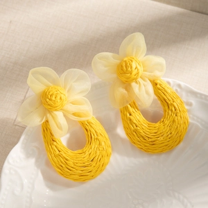 Detailed shot of yellow mesh flower earrings with woven raffia pendant on a white plate