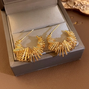 Macro shot of gold-plated twisted wire C-shaped earrings on a grey jewelry box