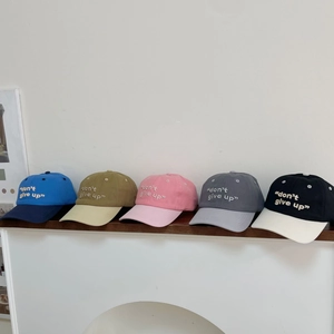 Detalle de cinco gorras de béisbol de algodón con bordado dont give up en una repisa blanca