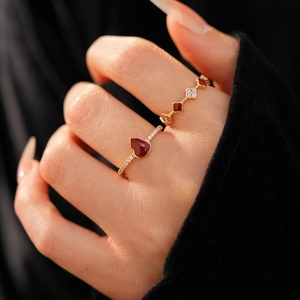 Detailed view of 18k gold plated clover and heart rings with red enamel on fingers
