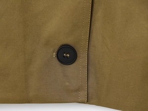 Close-up of matte black four-hole button with cross-stitching on khaki pleated jacket
