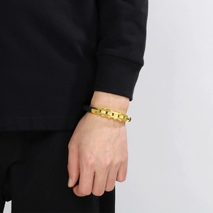 Close-up of gold industrial chain bracelet with black braided rope on male wrist